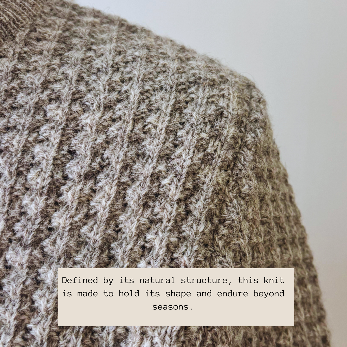 Close-up of a chunky knit sweater in a heathered taupe and cream yarn, showing the ribbed texture and a text overlay that reads, 'Defined by its natural structure, this knit is made to hold its shape and endure beyond seasons.'.